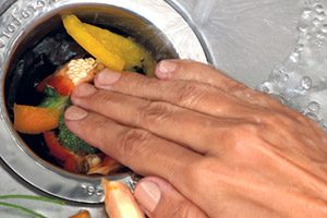 man pushing food down the sink drain, causing it to clog