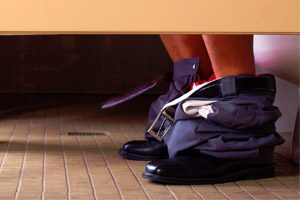 feet of a man wearing nice shoes, currently using the toilet in a public bathroom