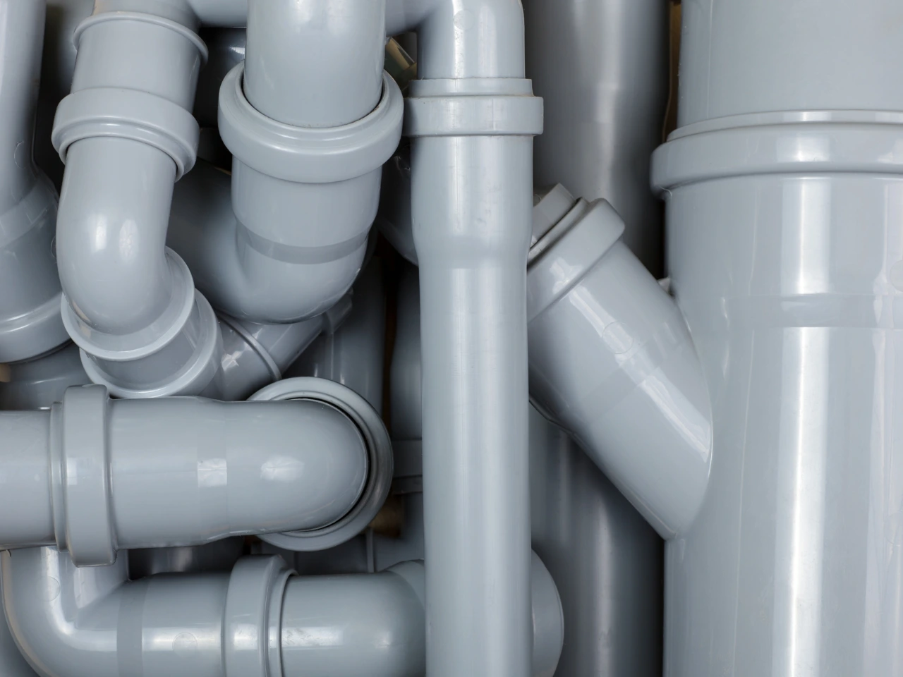 A close-up view of several interconnected gray PVC plumbing pipes with various bends, joints, and fittings arranged tightly together.
