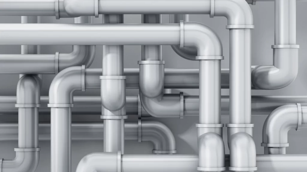 A complex network of shiny, silver metal pipes with multiple bends and joints, creating an intricate, interconnected pattern against a plain grey background.