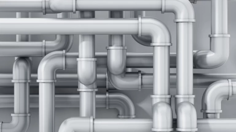 A complex network of shiny, silver metal pipes with multiple bends and joints, creating an intricate, interconnected pattern against a plain grey background.