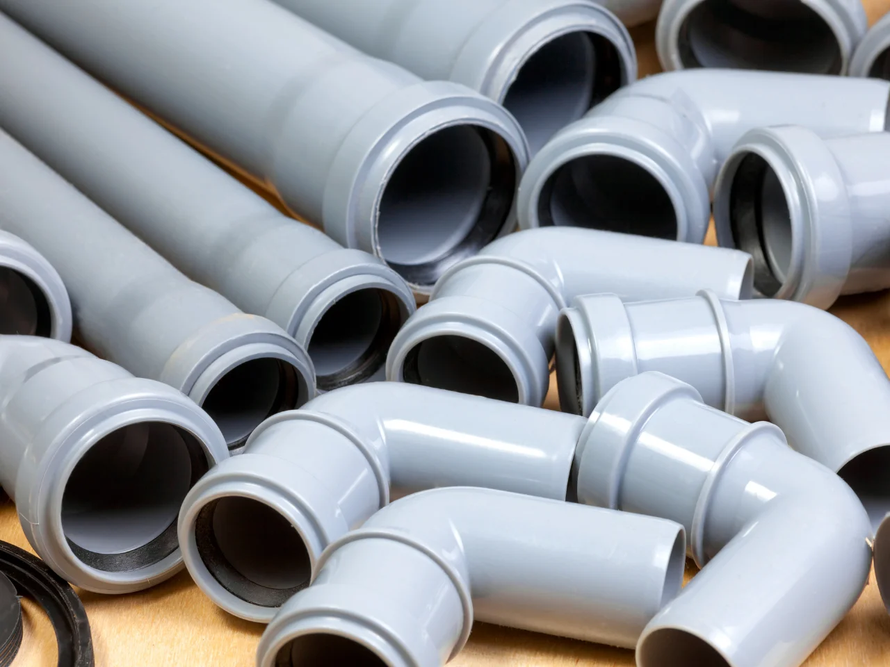 A collection of grey PVC plumbing pipes and elbow fittings are arranged on a surface, showing various sizes and angles.