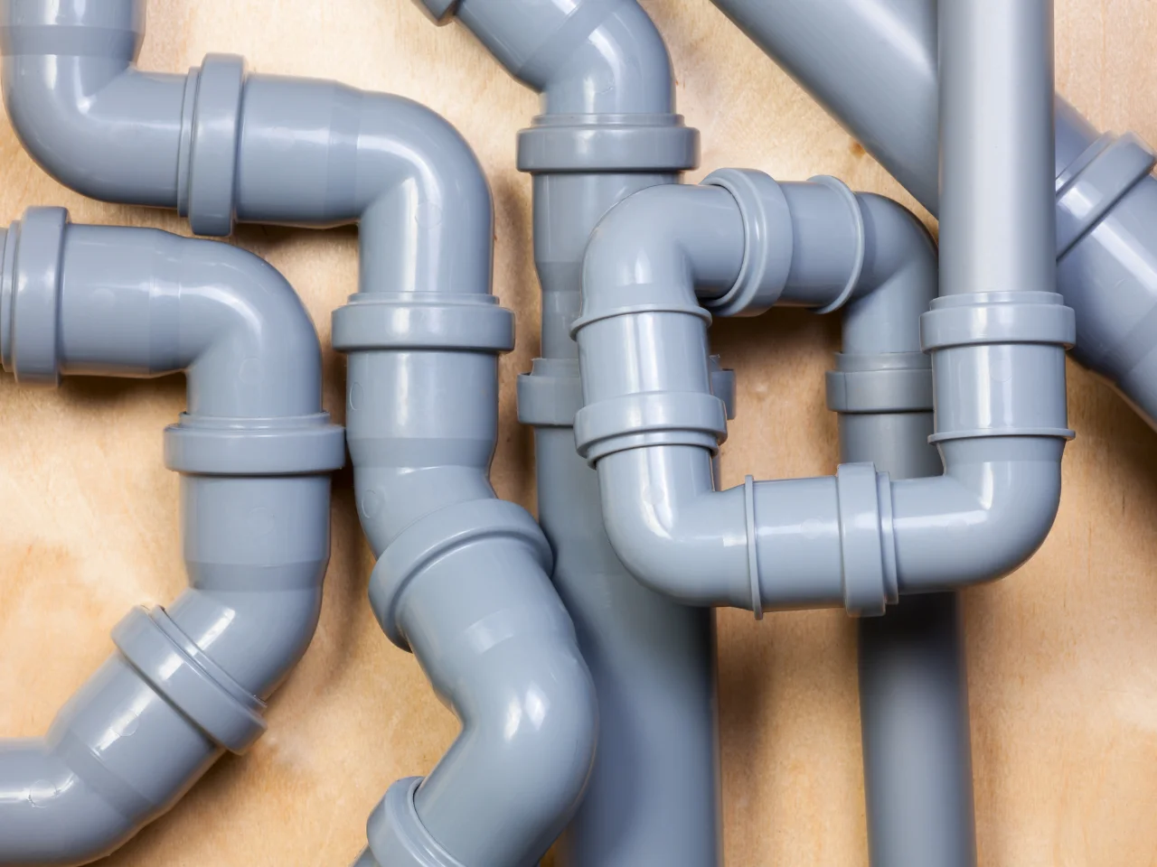 A close-up view of multiple gray plastic plumbing pipes with bends and joints, mounted on a wooden surface.