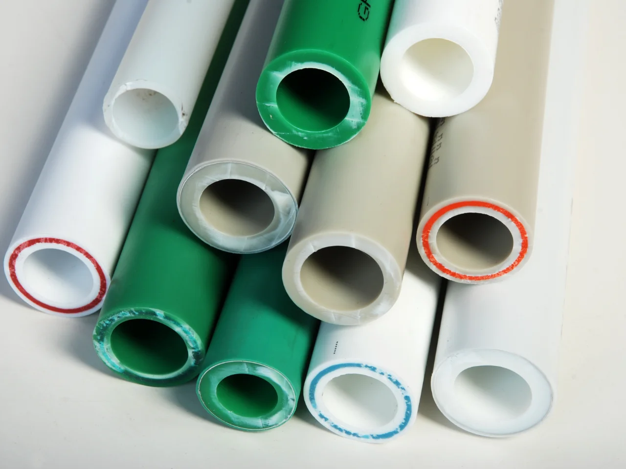 A stack of colored plastic pipes, including green, white, and gray, arranged horizontally with their open ends facing forward, showing different colored rims around some pipe openings.