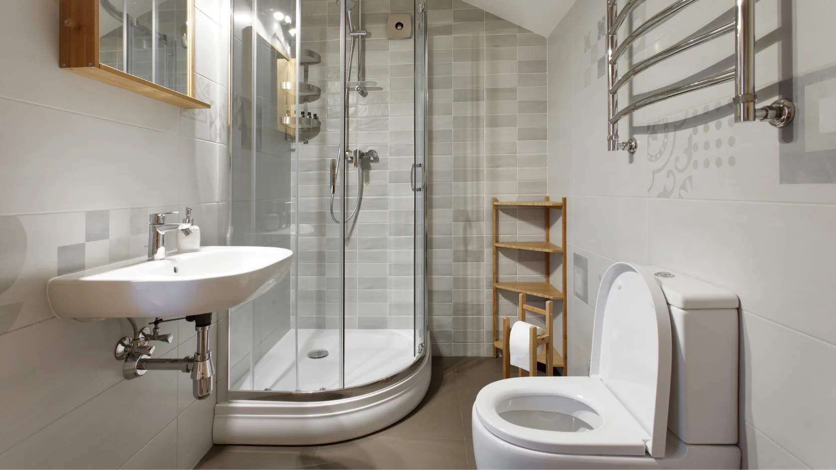 Modern bathroom with a glass-enclosed corner shower, white sink, toilet, wall-mounted towel rack, wooden shelving unit, and light grey tiled walls and floor.