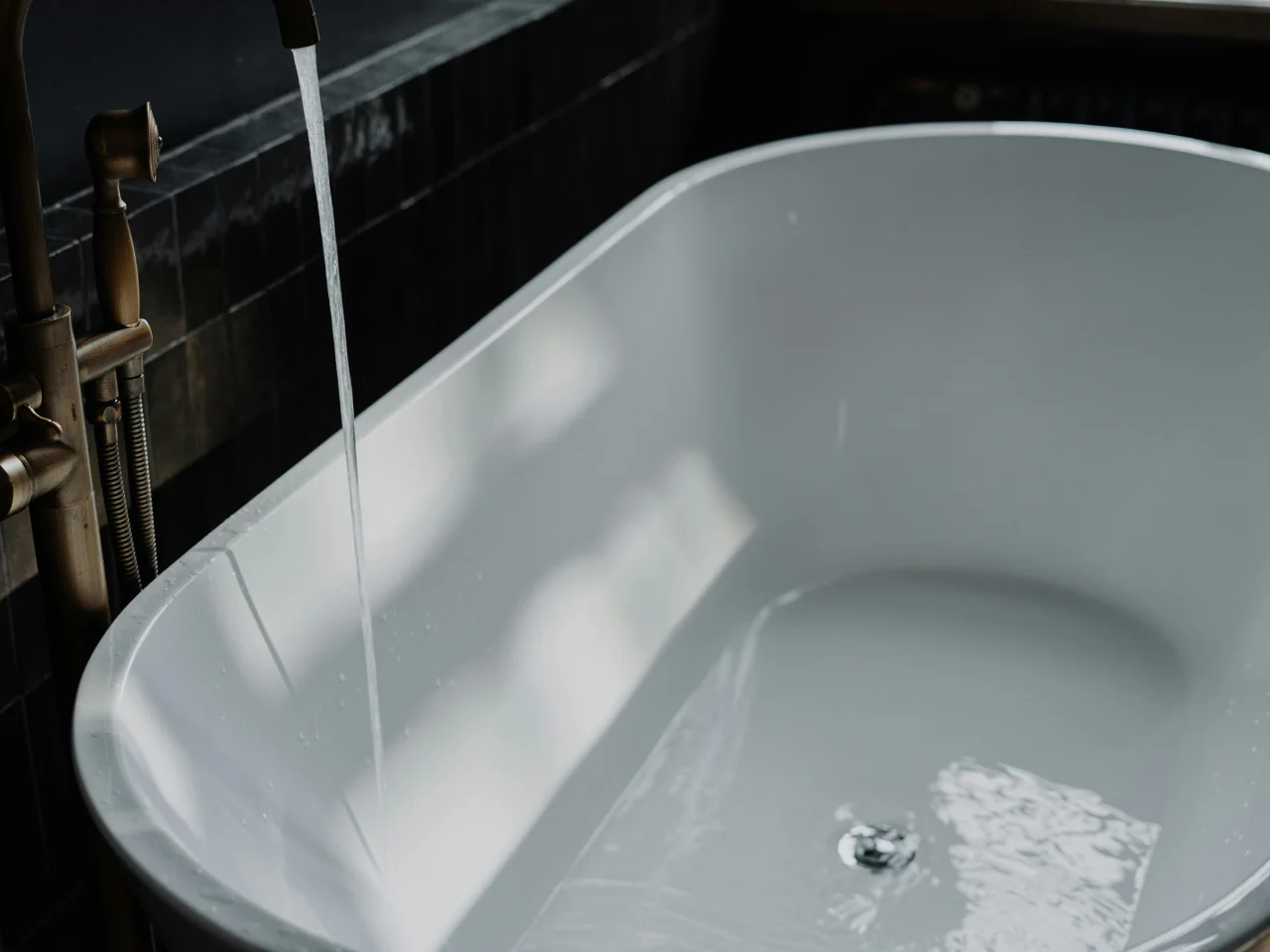 Close-up of water flowing from a faucet into a modern white bathtub, partially filled with water. Light reflections are visible on the water’s surface and the surrounding white tub.