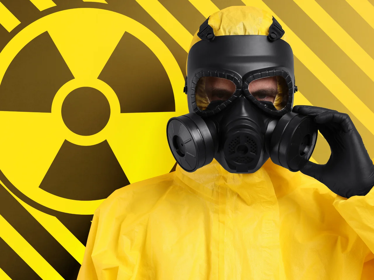 A person wearing a yellow hazmat suit and a black gas mask stands in front of a background featuring a large radiation warning symbol with yellow and black diagonal stripes.