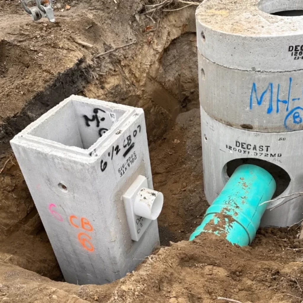 Two large concrete utility vaults, linked by a blue-green PVC pipe, are partially buried in exposed soil. The labeled vaults highlight essential infrastructure often seen during drain service Etobicoke professionals provide.