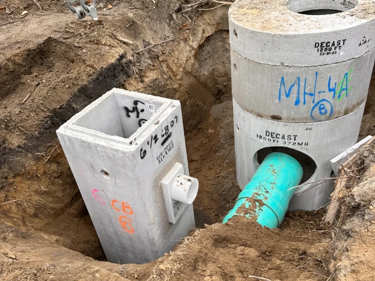 Two large concrete utility vaults, linked by a blue-green PVC pipe, are partially buried in exposed soil. The labeled vaults highlight essential infrastructure often seen during drain service Etobicoke professionals provide.