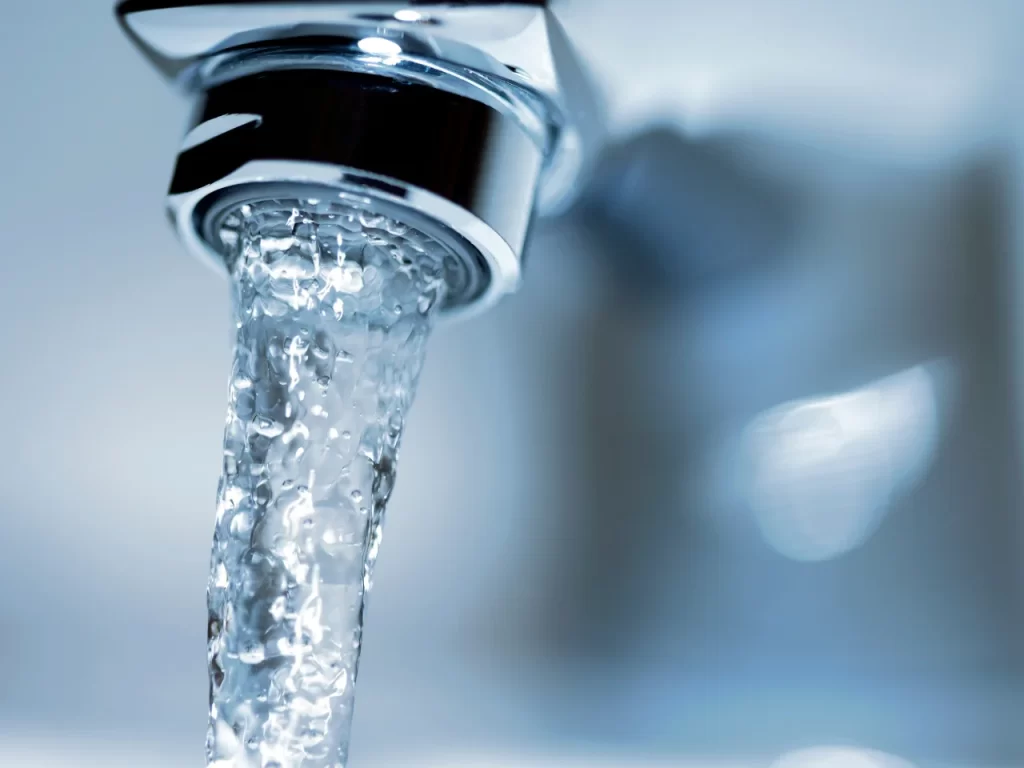 Close-up of clear water flowing from a shiny metal faucet, with a soft blue and white background, creating a fresh and clean appearance.
