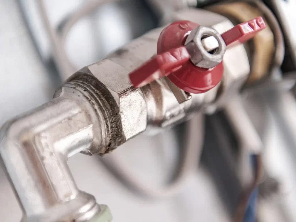 Close-up of a metal pipe with a red valve handle, showing details of the plumbing fixture and connected joints, with a blurred background.