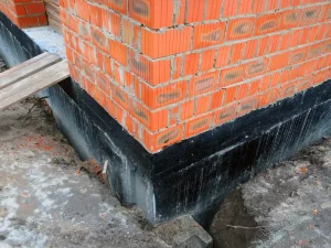 Corner of a brick building with a black waterproof coating applied to the foundation; the ground is partially excavated, revealing the base—ideal for assessing drain repair and plumbing in Toronto.