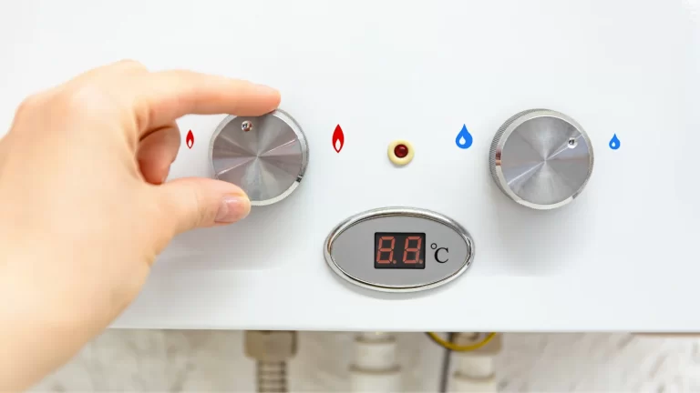 A hand is adjusting the temperature control knob on a water heater, which has two metal dials for hot and cold water and a digital display showing the temperature in degrees Celsius.