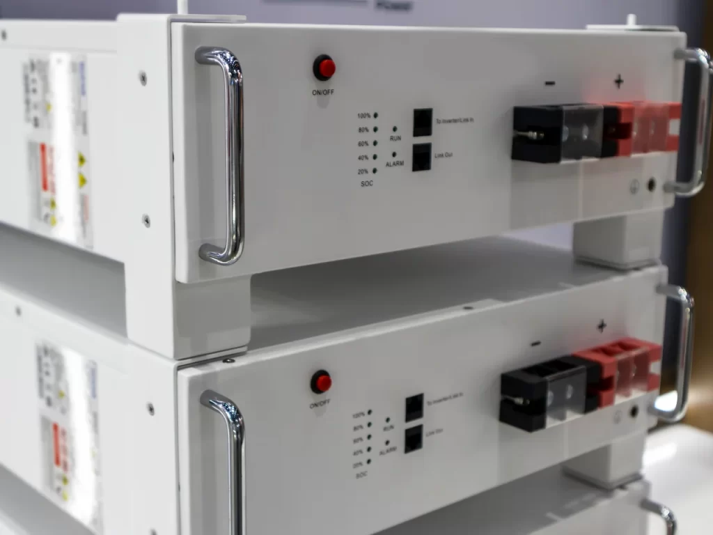 Two stacked white battery storage units with control panels, indicator lights, switches, and handle bars on the sides. The panels display status indicators such as SOC, ALM, RUN, and power levels.