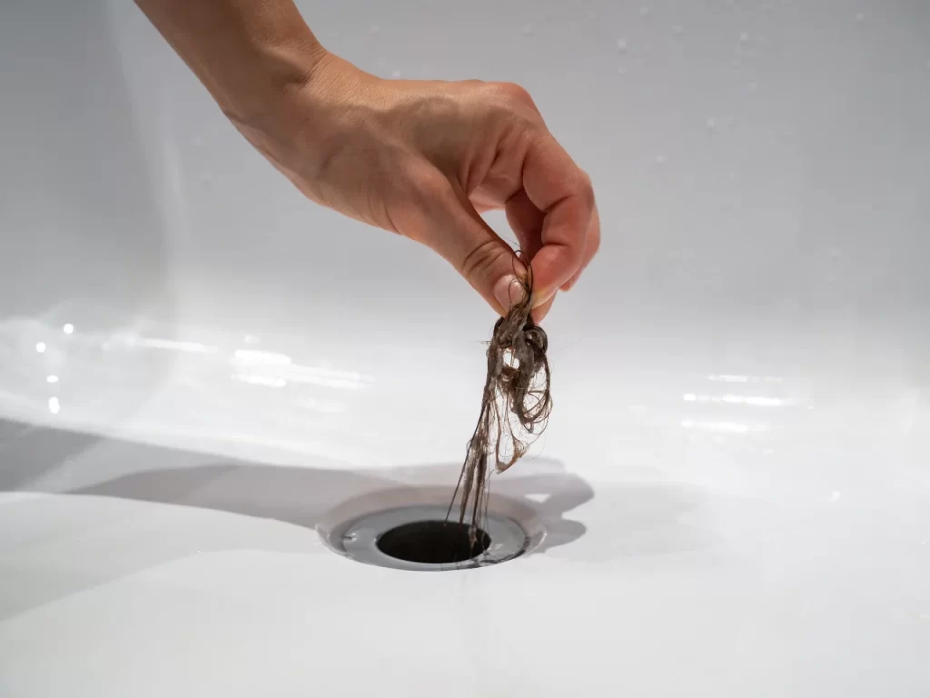 A hand removes a tangled clump of hair from a white sink drain.