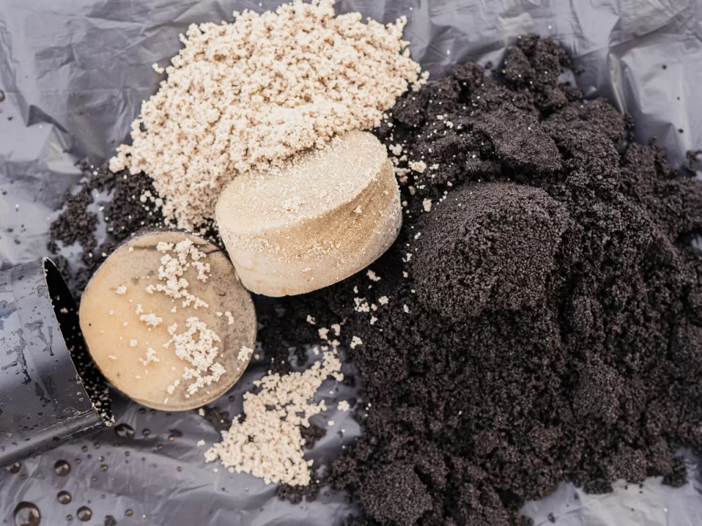 Close-up of light and dark soil piles, with two round soil blocks and a tipped-over black plastic plant pot on a plastic sheet.