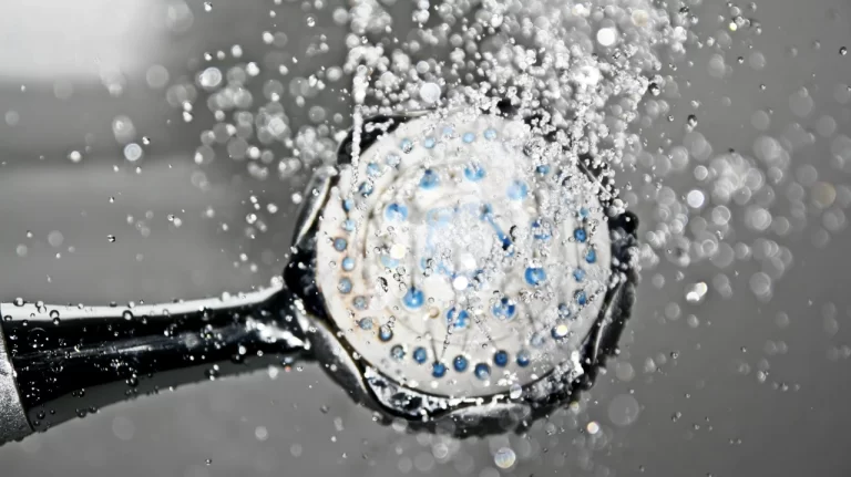 Close-up of a handheld showerhead spraying water, with droplets captured in motion and bokeh effect in the background, creating a dynamic and refreshing scene.