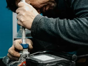 A person in a dark long-sleeve shirt tightly grips a pipe wrench to adjust a pipe fitting near a black battery, focusing intently on plumbing in Toronto and ensuring expert drain repair work.