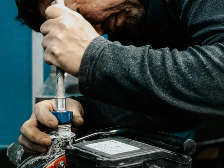 A person in a dark long-sleeve shirt tightly grips a pipe wrench to adjust a pipe fitting near a black battery, focusing intently on plumbing in Toronto and ensuring expert drain repair work.