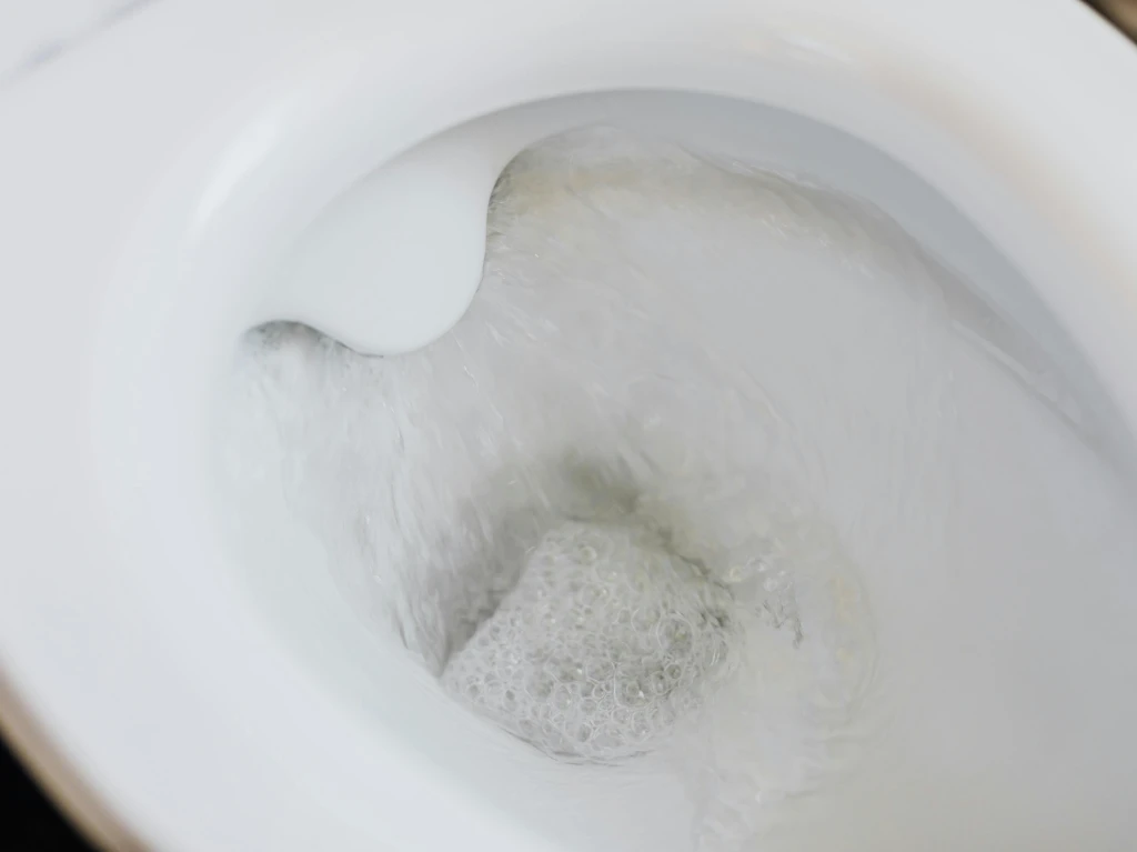Close-up view of a white toilet bowl being flushed, with swirling water and bubbles visible inside.
