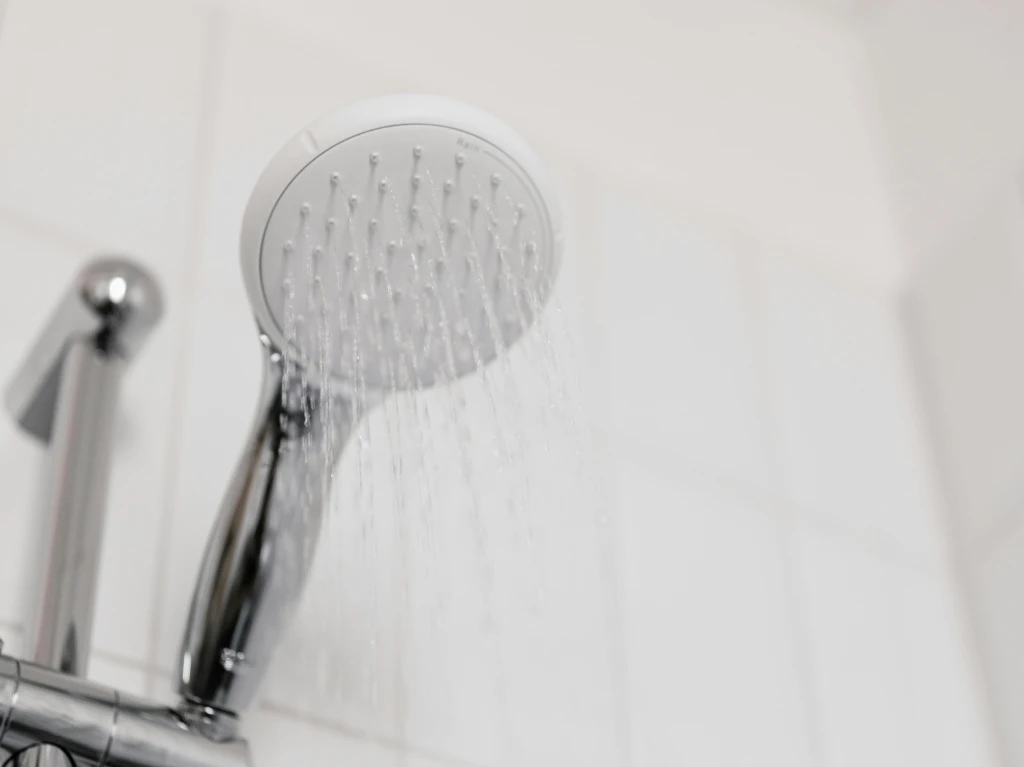 A modern handheld showerhead sprays water in a bathroom with white tiled walls.