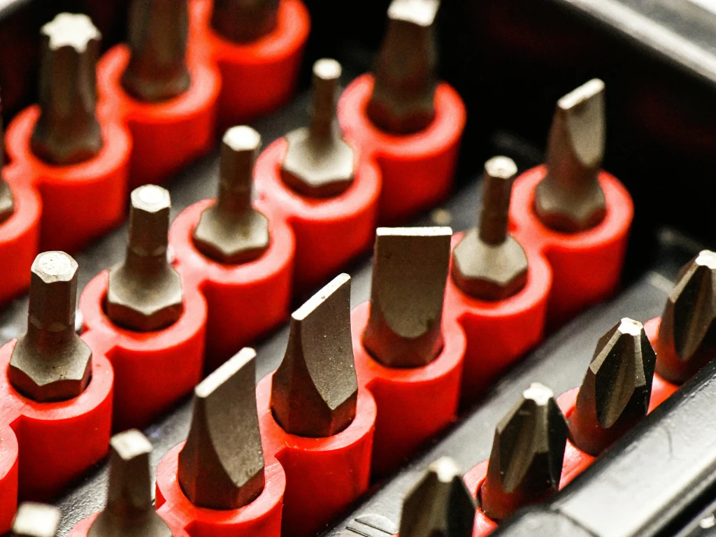 Close-up of various screwdriver bits arranged upright in a red plastic holder, showing different shapes and sizes, including flathead, Phillips, and hex bits, all stored in an organized manner.